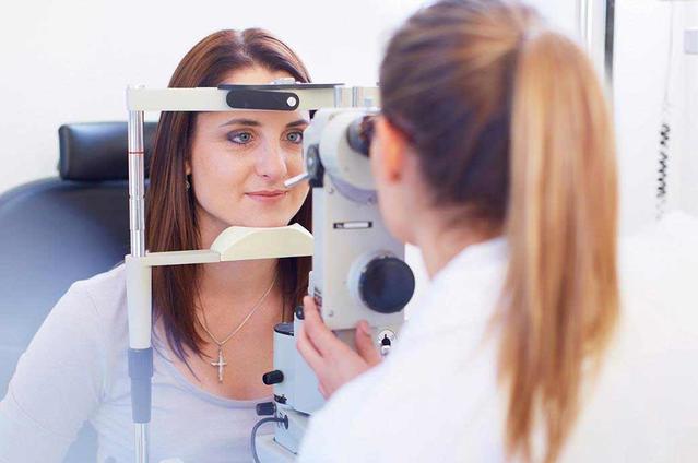 Plan d'une jeune femme regardant à travers une caméra rétinienne pendant que l’ophtalmologue regarde de l'autre côté.